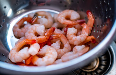 Close and selective focus on raw king prawns in a colander being cleaned and rinsed to make a home made prawn curry