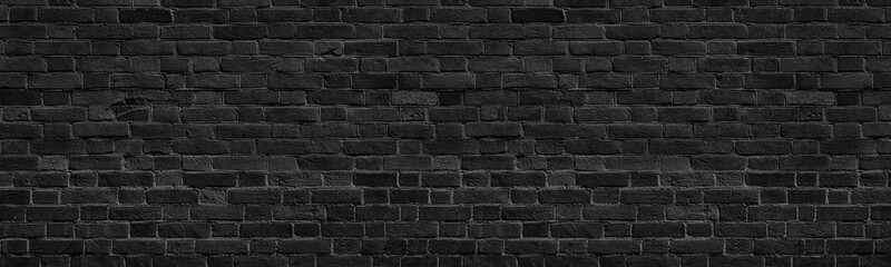 Old black shabby brick wall wide panoramic texture. Dark grey rough masonry. Aged brickwork...