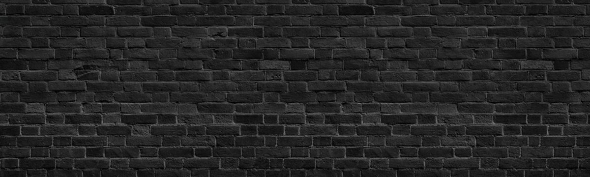 Old black shabby brick wall wide panoramic texture. Dark grey rough masonry. Aged brickwork panorama. Abstract grunge background
