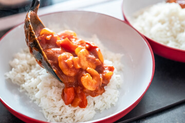 Close up of a spoon of home cooked king prawn curry being pured over a bed of freshly steamed basmati rice