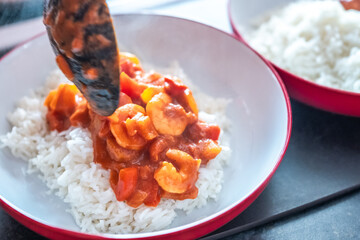 Close up of a spoon of home cooked king prawn curry being pured over a bed of freshly steamed basmati rice