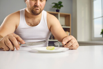 Fat guy sticking to strict diet eats too little food. Sad chubby young man sitting at table looking...