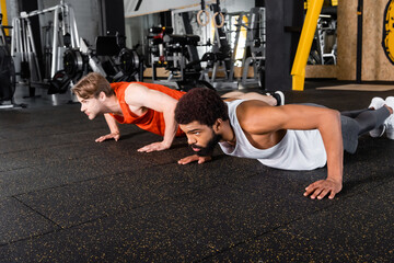 Fototapeta na wymiar young interracial sportsmen doing push ups on floor in sports center