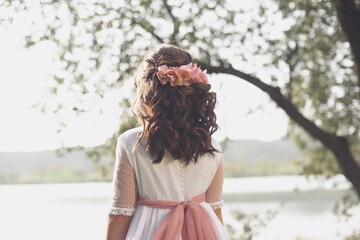 Girl in communion dress with her back facing the lake in nature