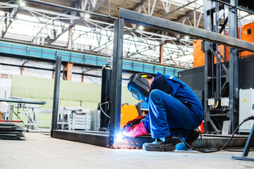 A welder at an industrial enterprise welds metal structures from an iron profile. Unrecognizable person. Copy space