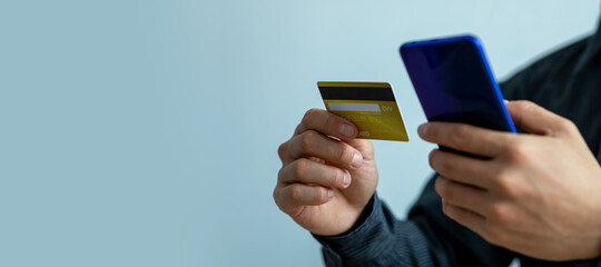 Close up of man hand using credit card and smartphone for buying online shopping with blue isolated background, 