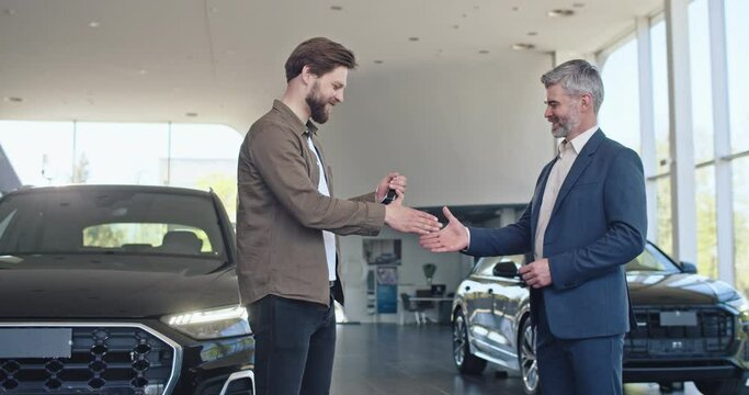 Caucasian car consultant presentating keys from new car to male client at salon. Happy young guy buying new transport. Selling and business concept.