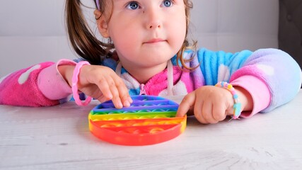 cute little girls with pop it sensory toy circle form. little female presses colorful rainbow squishy soft silicone bubbles on white background. Stress and anxiety relief. Trendy fidgeting game.