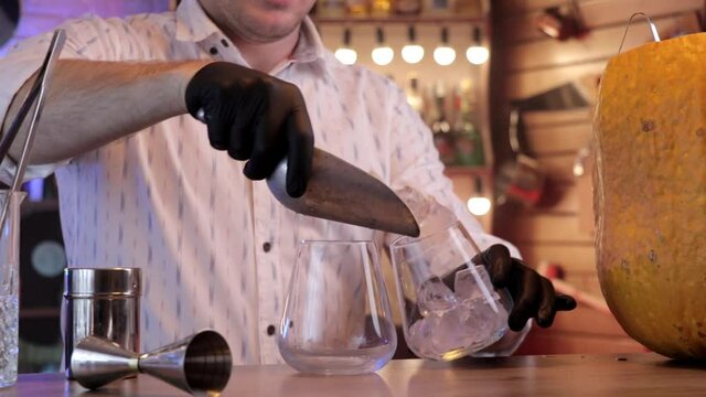 the bartender puts ice in the glass to prepare a cocktail