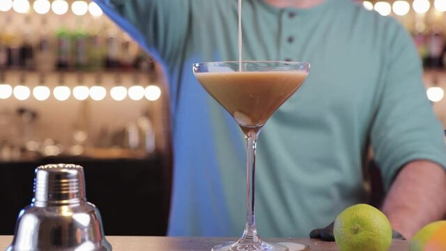 the bartender pours the cocktail into a martini glass .