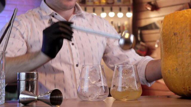 the bartender pour a cocktail  with a spoon  into the  glass.