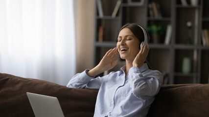 Happy relaxed attractive young woman listening favorite music in wireless headphones, enjoying...