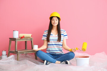 Young woman with rollers and cans of paint meditating near color wall