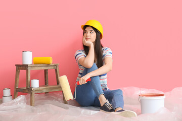 Young woman with rollers and cans of paint near color wall