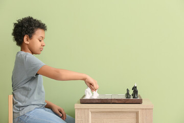 Cute African-American boy playing chess on color background
