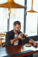 Handsome young man in casual clothing enjoying beer and smiling while spending time in the pub