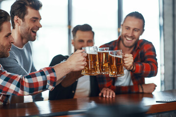 Happy young men in casual clothing toasting each other with beer and smiling