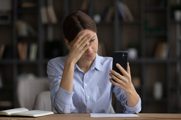 Frustrated young woman looking at cellphone screen, feeling nervous of getting message or email with bad news, upset female entrepreneur manager employee having problems with gadget, annoyed by spam.