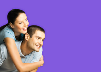 Portrait of standing close embracing smiling couple in blue casual clothing, love studio concept, isolated on violet colour background. Young brunette man and woman posing together. Copy space area.