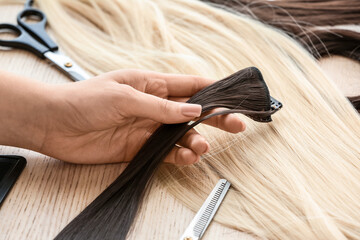 Female hairdresser with strand of brunette hair in beauty salon, closeup