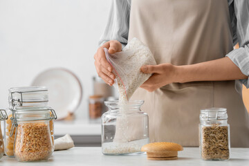 Woman pouring rice into jar in kitchen