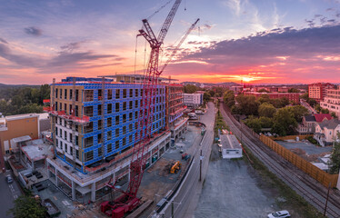 Aerial view of office building, apartment complex construction site in downtown Charlottesville Virginia with red cranes standing still against the setting sun that paints the sky red, yellow, orange 