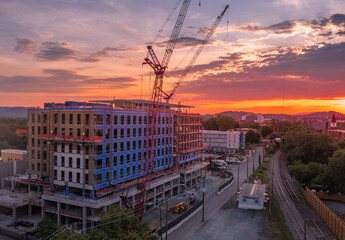 Aerial view of office building, apartment complex construction site in downtown Charlottesville Virginia with red cranes standing still against the setting sun that paints the sky red, yellow, orange 