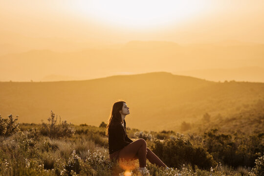 Serene woman sitting on hill in mountains at sunset