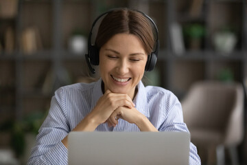 Smiling young business lady ceo manager in headset with mic looking at computer screen, holding...