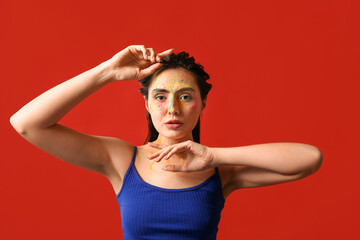 Beautiful young woman with paint on her face against color background