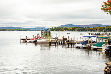 Petrol pump for boats at the end of a wooden pier in a marina on a lake under cloudy sky in autumn. Colourful autumn trees are visible on the other side of the lake. Tranquil scene.