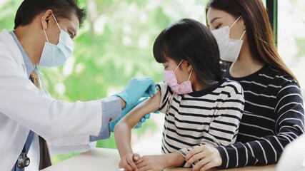 Asian senior doctor wearing gloves and isolation mask is making a COVID-19 vaccination in the shoulder of child patient with her mother at hospital. - Powered by Adobe