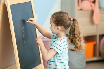 Fototapeta na wymiar Little girl drawing on blackboard in room