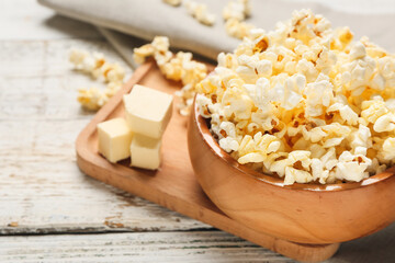 Bowl with tasty popcorn and butter on light wooden background