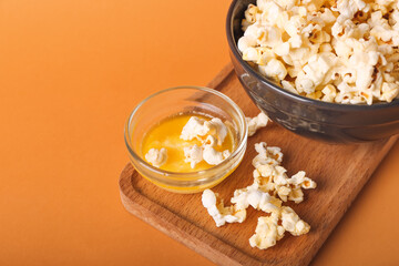Bowls with tasty popcorn and butter on color background