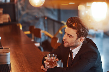 Top view of handsome young man in full suit having alcohol drink