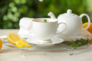 Grid with cup of tasty green tea, pot and ingredients on table outdoors