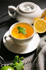 Tray with cup of tasty green tea, pot and ingredients on dark table