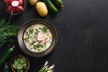 Summer freshness Russian cold soup Okroshka with kefir or airan and raw vegetables ingredients on a black background. View from above. Copy space.