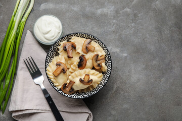 Bowl with tasty dumplings, onion and sour cream on grunge background