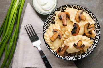 Bowl with tasty dumplings, onion and sour cream on grunge background