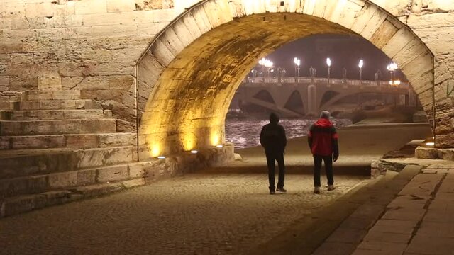 People walking under Stone Bridge archway at night in Skopje, Macedonia.