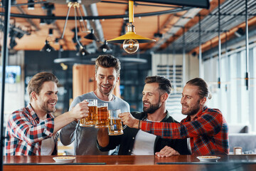 Group of happy young men in casual clothing toasting each other with beer and smiling