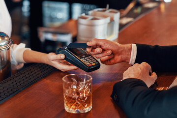 Top view close-up of man making a contactless payment while sitting at the bar counter in restaurant