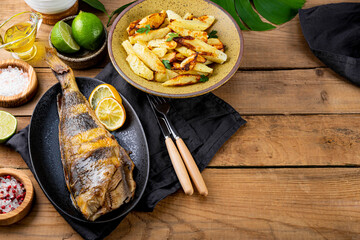 Baked sea bass or lingcod fish with potatoes on the wooden table, copy space for text