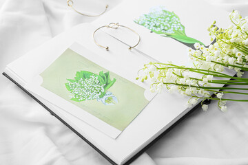 Beautiful lily-of-the-valley flowers, book and greeting card on light fabric background