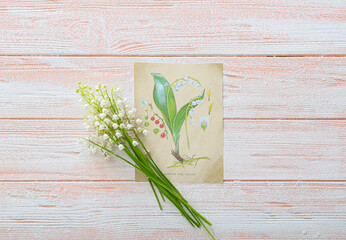 Beautiful lily-of-the-valley flowers and greeting card on wooden background