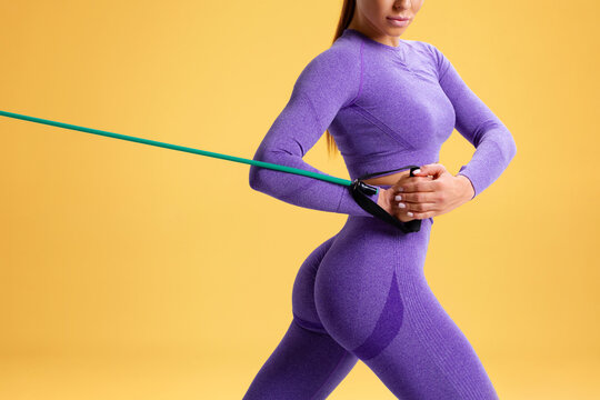 Athletic girl working out with resistance band on orange background. Fitness woman exercises with expander