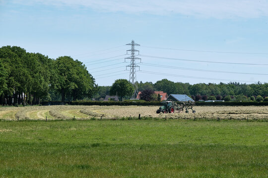 Dronten, the Netherlands June1,2021:Grassland with tractor mower and rake, grass ready to be ensiled.Dutch farmers race against the rain to hay,mow, rake and silage.All farmers are working on the land
