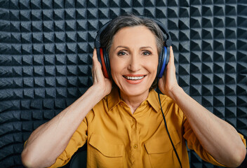 Hearing loss treatment. Positive mature woman wearing audiometry headphones while hearing test and...